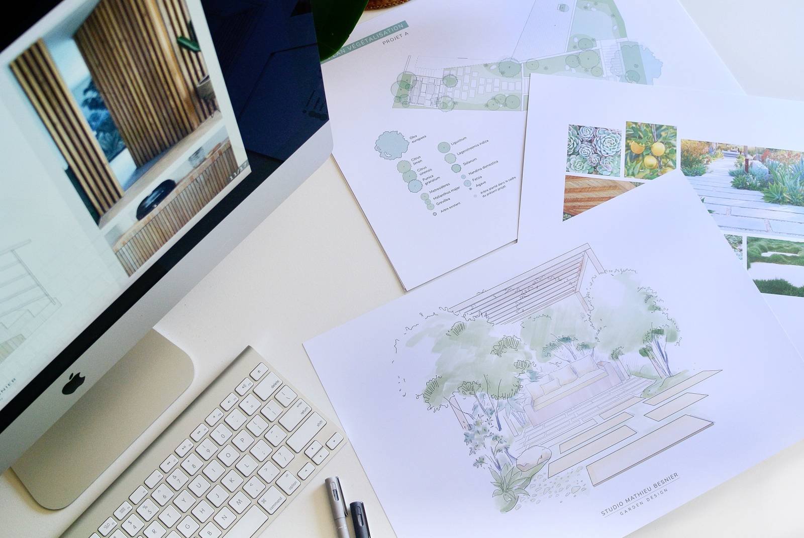 Bureau avec iMac affichant des intérieurs boisés, des plans de végétalisation Projet A, des photos de plantes et un croquis de jardin du Studio Mathieu Besnier.