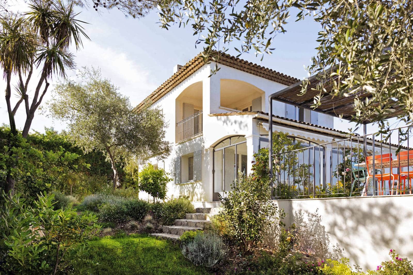 Villa blanche style méditerranéen avec toit en tuiles, entourée d'un jardin luxuriant, d'oliviers et d'un escalier en pierre.